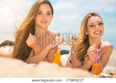 Gierlfriends drinking cold drink beverage having fun at beach party. Female babes in bikini enjoying orange water from glass boutle. summer concept
