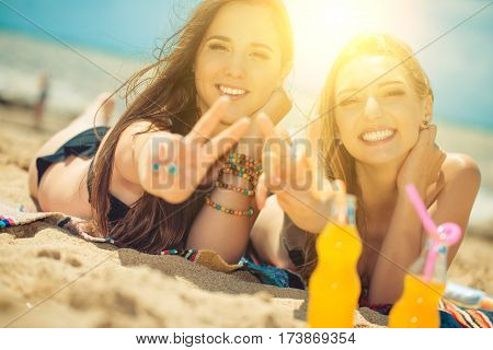 Gierlfriends drinking cold drink beverage having fun at beach party. Female babes in bikini enjoying orange water from glass boutle. summer concept