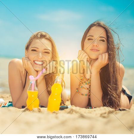 Gierlfriends drinking cold drink beverage having fun at beach party. Female babes in bikini enjoying orange water from glass boutle. summer concept