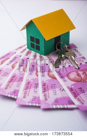 indian real estate or residential model house with new currency notes, keys, toy car and calculator, selective focus