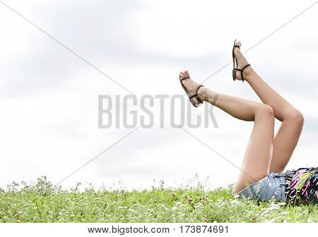 Low section of woman with feet up lying on grass against sky