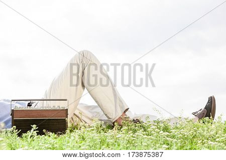 Low section of man lying by vintage radio on grass against clear sky