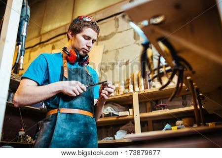 Young cabinetmaker processing wooden detail with chisel