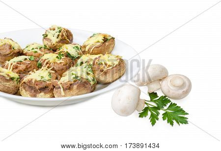 Baked button mushrooms stuffed with minced meat cheese and greens on the white dish and several uncooked mushrooms with parsley twig beside closeup on a light background