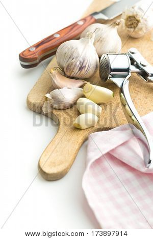 Garlic and garlic press on cutting board isolated on white background.