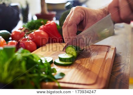 Crop shot of hands slicing cucumber on a cutting board. Healthy food. Preparing nutritious eating. Close-up of hands of chef cutting vegetables on wooden table