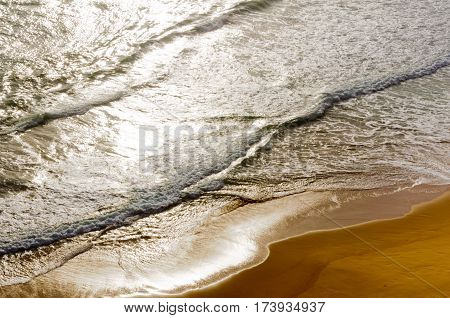 Gentle waves lit by sunshine awash the sandy beach