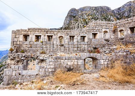 Old stone walls of medieval fortification, town ruins against Lovcen mountain in Kotor, Montenegro.