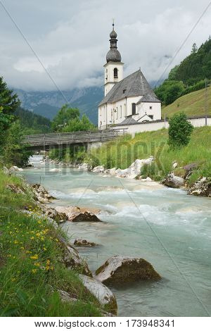 Parish church of Saint Sebastian in Ramsau Germany with the Bavarian Alps in the background and the river Ramsauer Ache in the foreground. Built in 1512