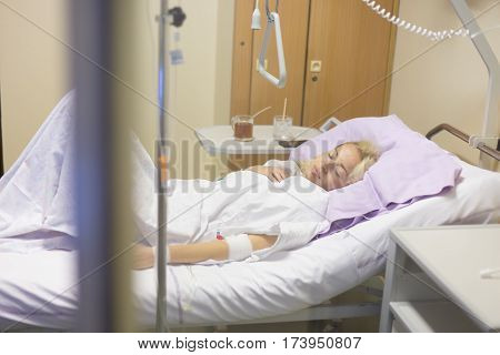 Bedridden female patient lying in hospital bed, recovering after surgery.