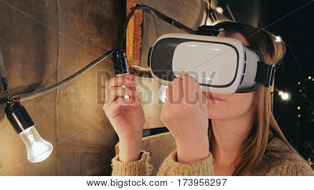 Young woman using Virtual Reality Glasses. Virtual reality mask. VR. Retro loft Christmas background with light bulbs. Close up shot