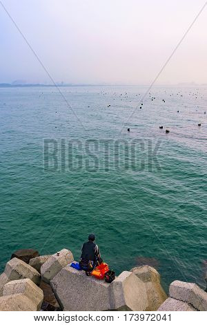 TAIPEI TAIWAN - JANUARY 05: Fisherman sitting alone fishing on rocks in the Tamsui area of Taipei on January 05 2017 in Taipei