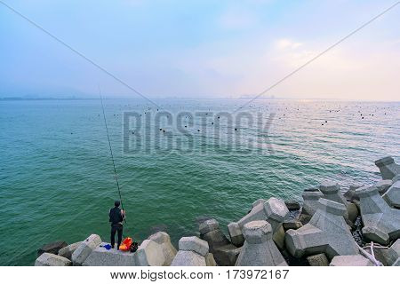 TAIPEI TAIWAN - JANUARY 05: Fisherman alone trying to catch fish along the rocky seafront in the Tamsui area of Taipei on January 05 2017 in Taipei