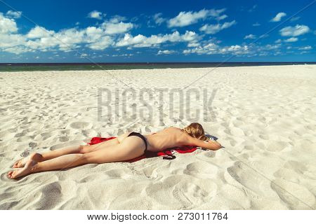 Single Topless Young Woman In Swimsuit At Sand Sea Beach With Blue Sky And Clouds Tanning Lying