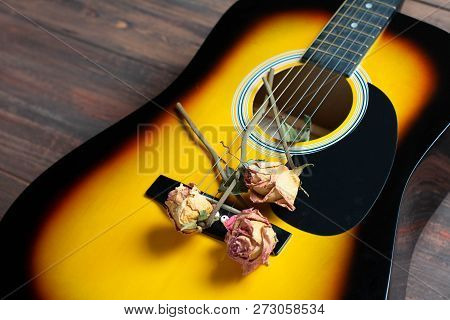 Acoustic Guitar With Dried Roses On The Wooden Table. Template For Advertising A Concert Of Memory W