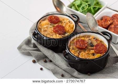 Slovak Christmas National Cabbage Soup In Two Small Black Pots With Sausage On The Tablecloth Backgr