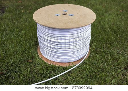 Top View Of Roll Of White Industrial Electrical Cable On Large Wooden Reel Isolated Outdoors On Gree