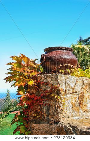 Still Life With Iron Vase And Leaves On Rhe Stone Wall And  Sea On The Background.
