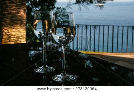 Two Glass Goblets With Water, Where Tere Is Reflexion Of Rhe Sea, Palm And Pine