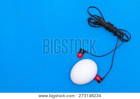 Chicken Egg And Headphones Isolated On Blue Background. Abtract Photo.