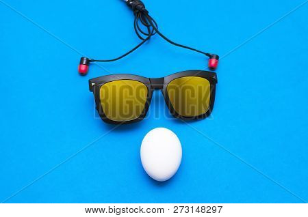 Chicken Egg, Sunglasses And Headphones On A Blue Background. Abstract Image.