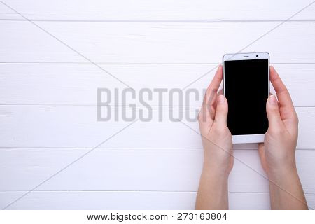 Female Hands Holding Mobile Phone With Blank Screen On White Wooden Table. Smartfone White