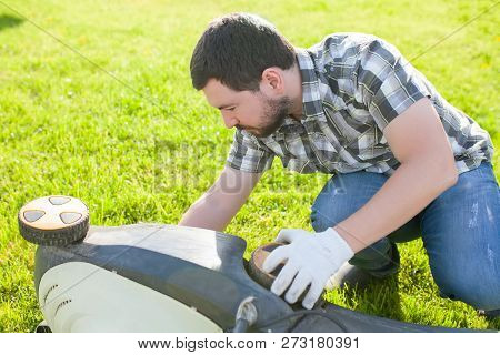 Man Cleaning Or Fixing Lawn Mower Blade Outdoora At The Grass.