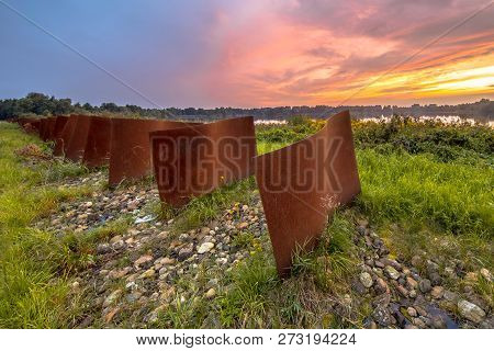 Row Of Rusty Metal Curved Objects In Landscape With Lake And Sunset At Piccardthofplas Groningen Cit
