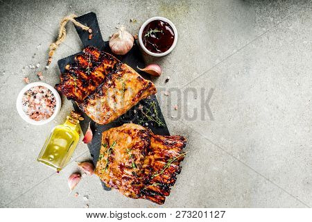 Grilled Meat Concept. Bbq Pork Ribs With Barbeque Sauce, Olive Oil. Fresh Herbs On Grey Stone Backgr