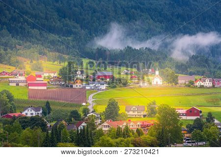 Norwegian Village Landscape With Low Fog Clouds, Mountains, Church And Colorful Houses In Olden, Nor