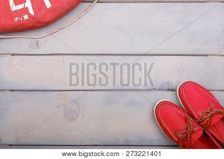 Red Boat Shoes On Wooden Background Near Lifebuoy And Rope. Top View. Copy Space
