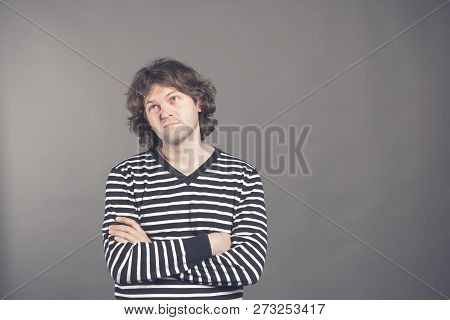 Studio Shot Of Pensive Young European Male With Voluminous Hair Posing At Blank Wall, Keeping Arms C
