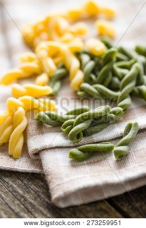 Uncooked spinach gemelli pasta on tablecloth.