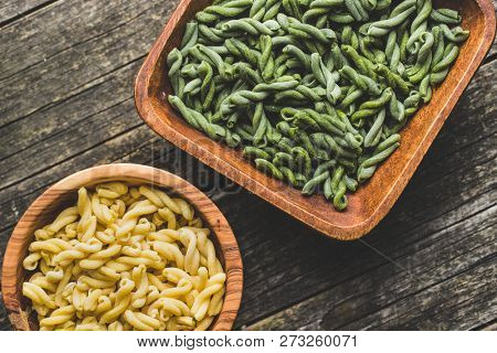 Uncooked spinach gemelli pasta in wooden bowl.