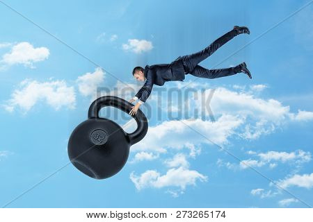 A Young Businessman In Mid Air Gripping Hold Of A Disproportionately Big Kettlebell With Number 32 O