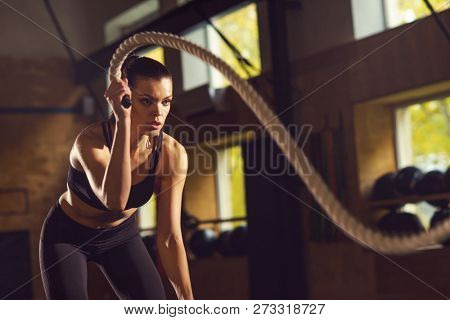 Fit, sporty and athletic sportswoman working in a gym. Woman training using battle ropes. Sports, athletics and fitness concept.