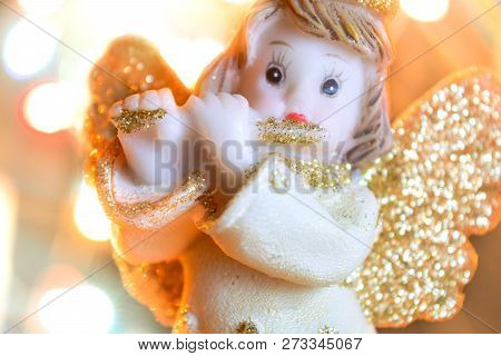 Figurine Of Little Angel With Golden Shiny Wings And Halo That Plays Flute On Shining Background Of 