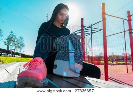 Woman Rummaging In Backpack After Exercising Outdoors In Urban Environment.