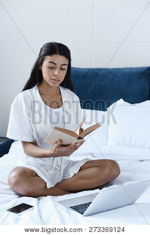 Beautiful Mixed Race Girl In White Robe Reading Book On Bed In Morning