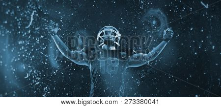 American football player standing with arms up against old weathered wall