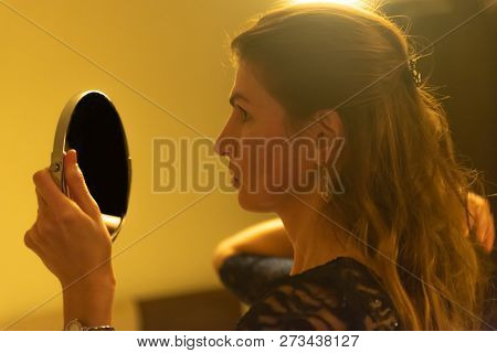 Elegant Young Female Dressed In Black Evening Dress Looking At Herself In The Mirror