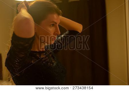 Elegant Young Female Dressed In Black Evening Dress Looking At Herself In The Mirror And Fixing Her 
