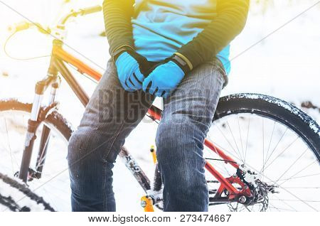Rider In A Blue Jersey And Blue Gloves Sitting On The Bicycle Frame In Snowy Forest. Rest During Tra