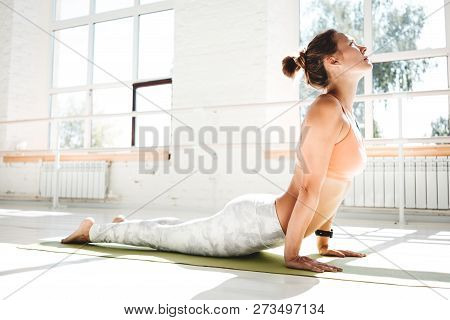 Taned Fit Woman Practicing Yoga Indoor White Class. Athletich Strong Girl Practice Cobra Asana In Su