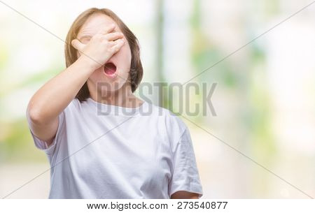 Young adult woman with down syndrome over isolated background peeking in shock covering face and eyes with hand, looking through fingers with embarrassed expression.