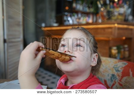 Little Girl Eating Fried Eggplant Slice In Restaurant