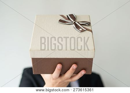 Unrecognizable Man Holding Gift Box With Brown Bow And Giving It To Camera. Close-up Of Man Presenti