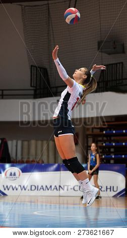 KAPOSVAR, HUNGARY â DECEMBER 2, 2018: Zsofia Harmath serves ball at a Hungarian National Championship volleyball game between Kaposvar (white) and Palota VSN (blue) in Sportcsarnok Kaposvar.