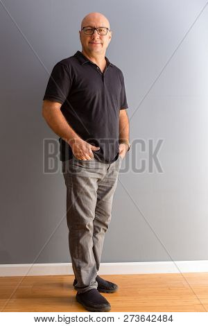 Full Length Portrait Of Adult Middle-aged Bold Man In Glasses, Wearing Black Polo And Grey Jeans, St