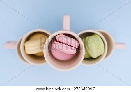 Three Macaroons Of Pink, Green And Yellow In Cups On A Blue Background.
